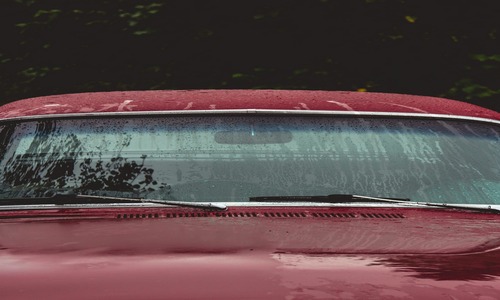 Raindrops on a red car's windshield and hood, showing possible aftermath of a hailstorm.