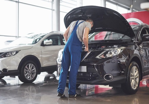 Alt text: Mechanic checks under hood of black SUV in modern auto service center.









