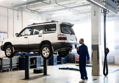 Alt text: Mechanic inspects lifted SUV in clean, well-lit auto repair shop.









