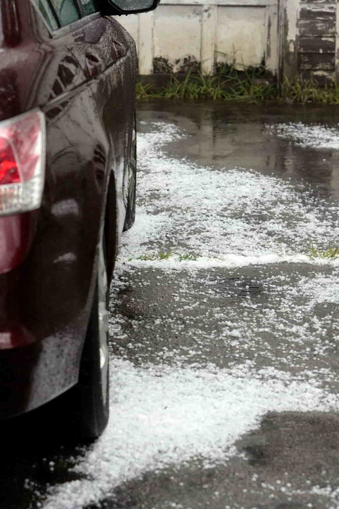 Close-up of a car and ground covered in hailstones after a storm in a residential area.