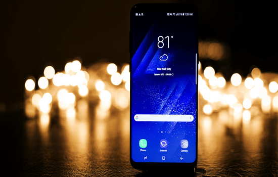 Smartphone displaying weather forecast with blurred lights in the background.