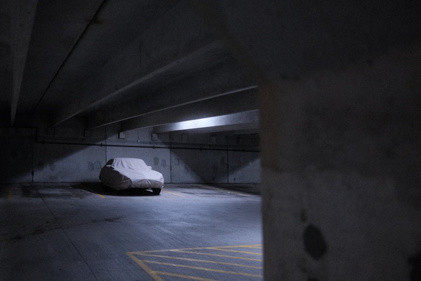Covered car parked alone in a dimly lit underground parking garage.